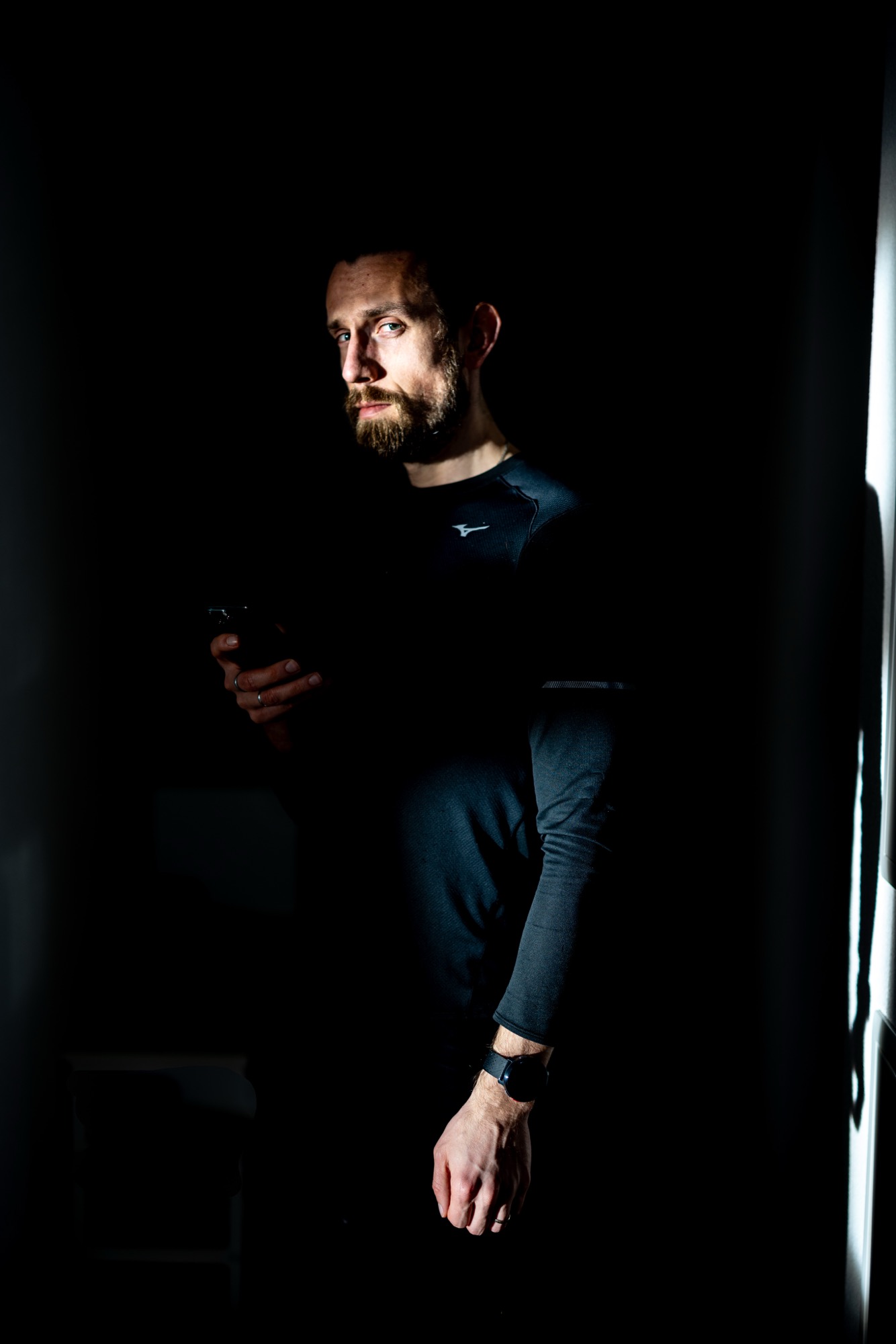Siarhei Thor in a dark long-sleeve athletic top, side-lit against a dark background, holding a phone.